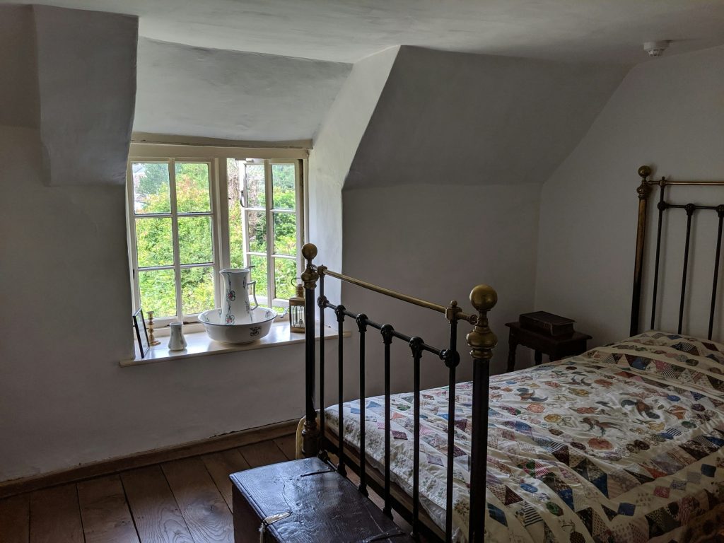 Before: a cottage bedroom with sloped ceilings, a dormer window, an old brass bed and a patchwork quilt