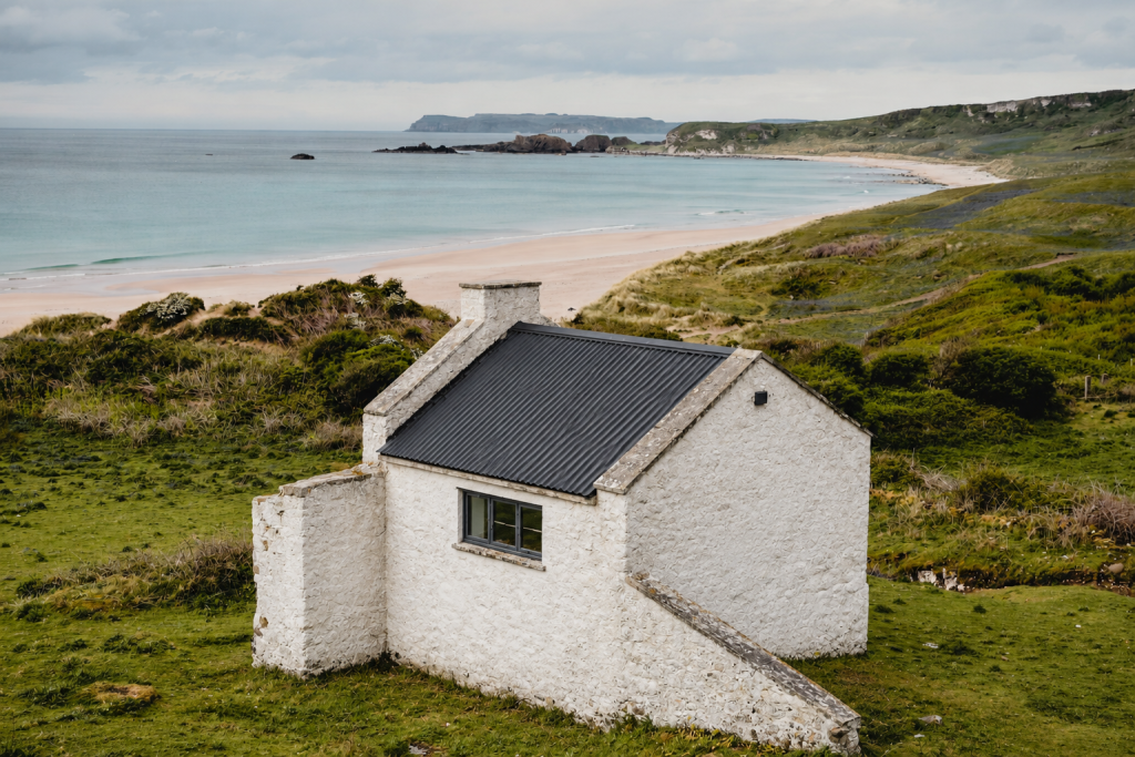 Concept: the same cottage restored with a new dark roof, fresh white render and a new window, with the same beach view