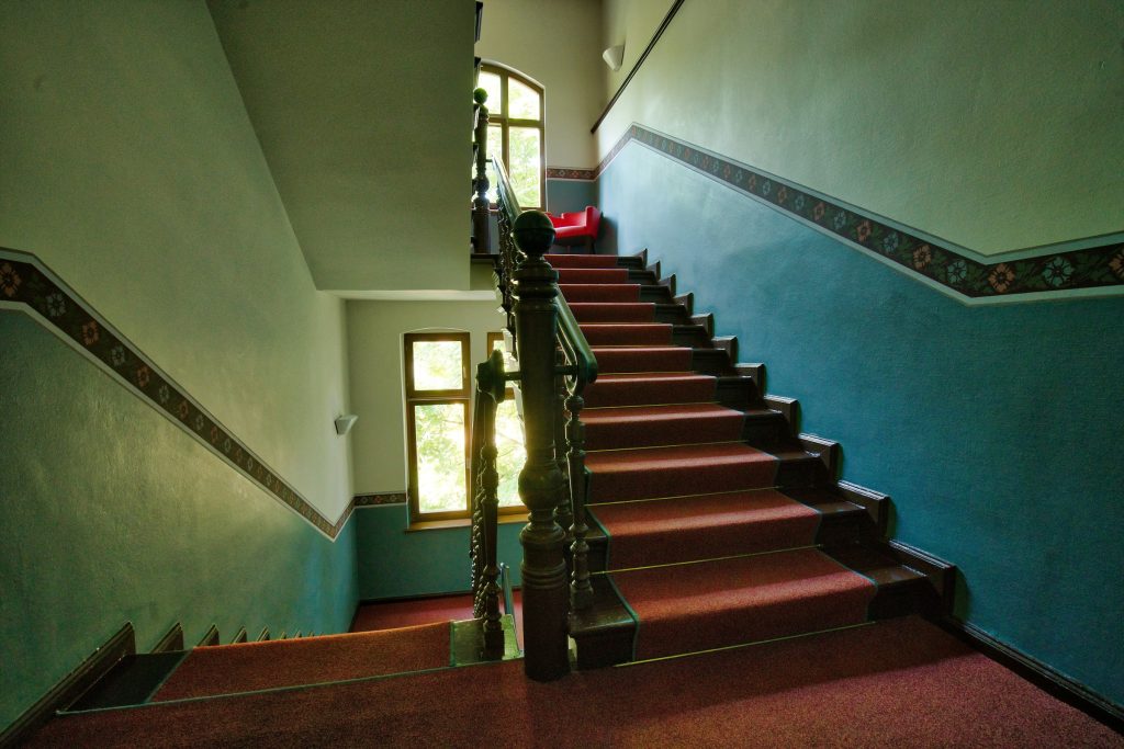 Before: a stairwell with dark teal walls, a patterned border, red carpet and a dark carved banister