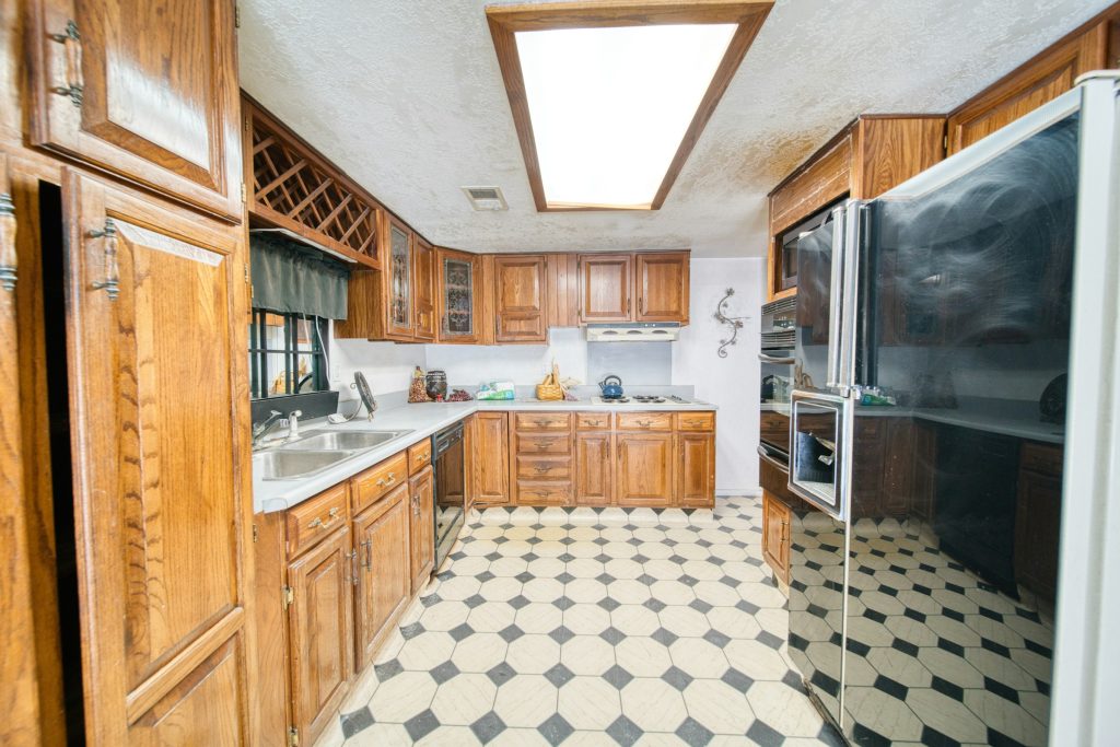 Before: a dated galley kitchen with orange oak units, a textured ceiling with a fluorescent light box and a checkered lino floor